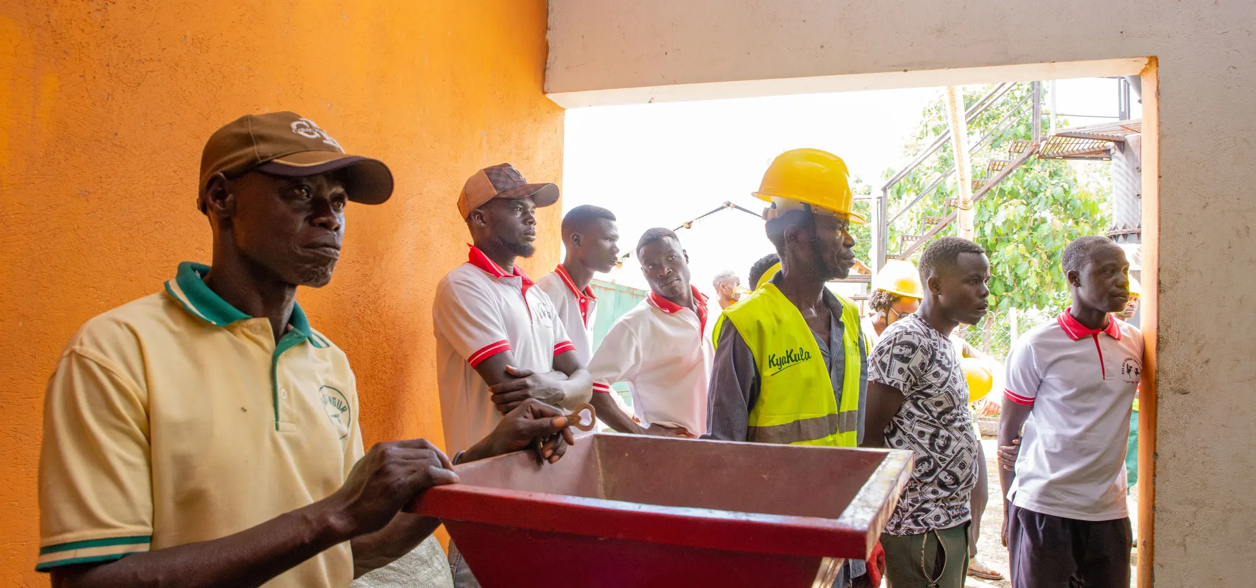 A worker tipping a bin of agricultural residue into the gasifier intake, watched by onlookers