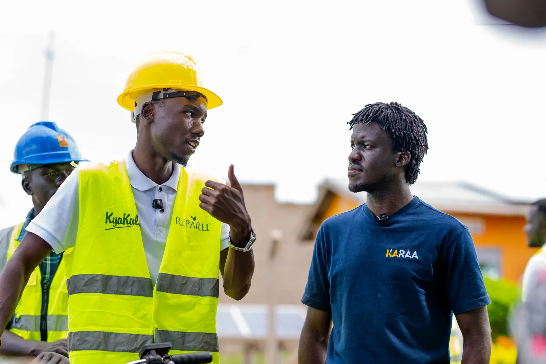 Two men in conversation at the Got Ngur site, one wearing project hi-vis