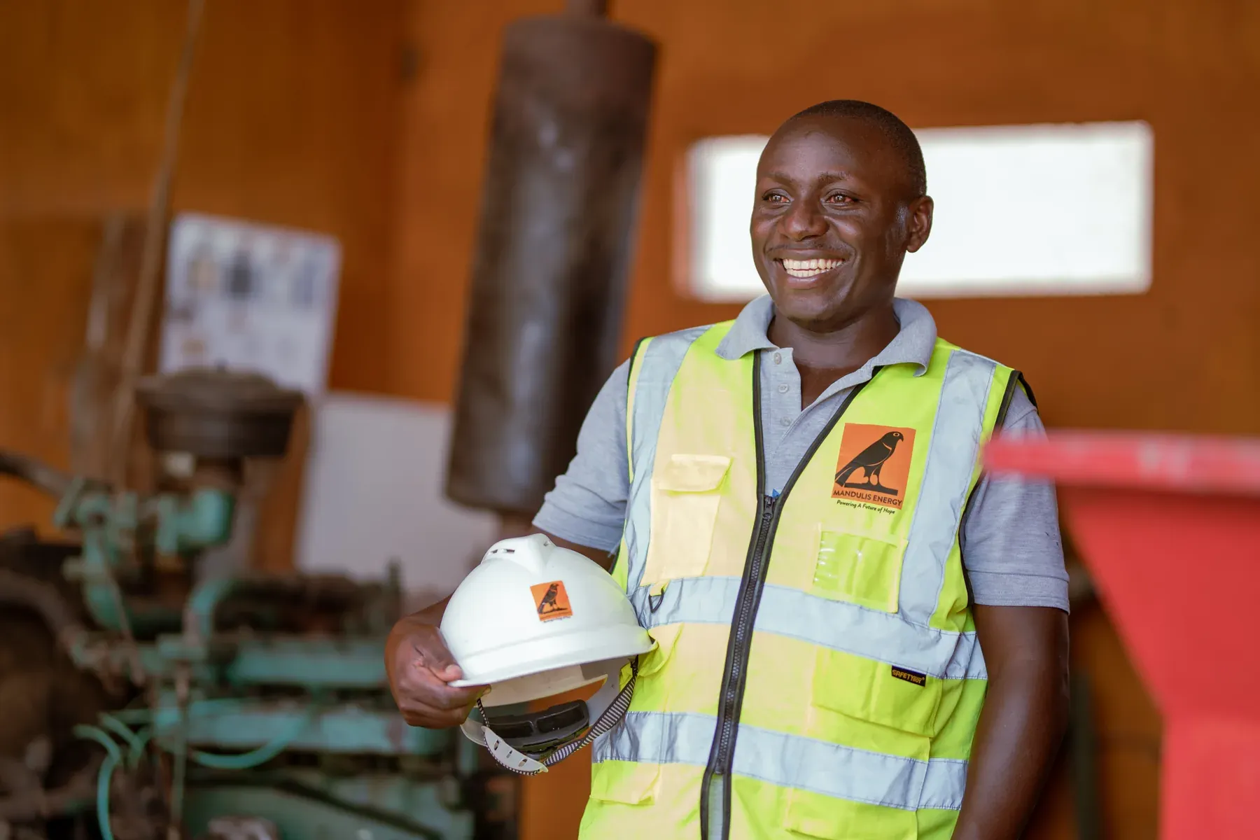 A Mandulis Energy technician holding his helmet beside the generator in the generation hall